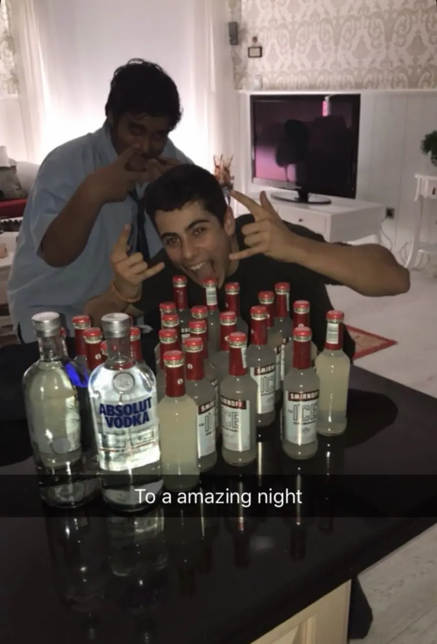 Party-era photo of two teenagers posing behind a table of bottles