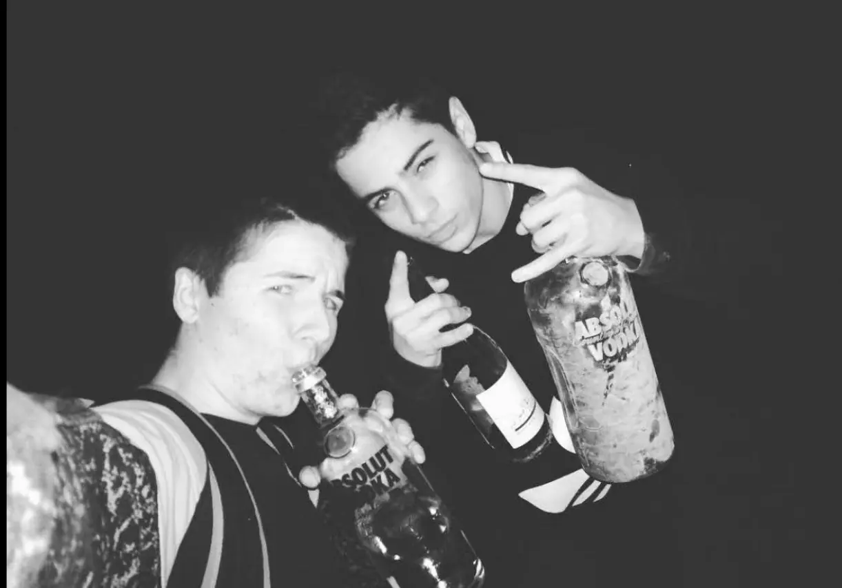 Black-and-white photo of two teenagers posing with bottles