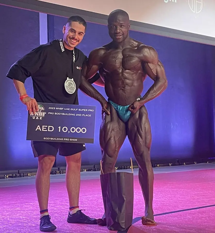 On stage with the prize board: 2023 WNBF UAE Gulf Super Pro, Pro Bodybuilding, 2nd place